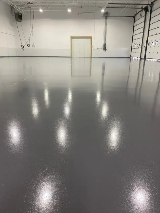 Empty gray garage with polished concrete floor and white walls, lit by overhead lights.