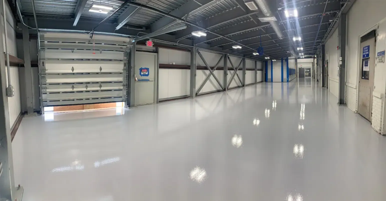 Empty industrial warehouse interior with polished white floor, metal walls, and overhead lights