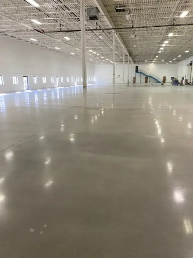 Empty indoor warehouse with polished concrete floor and high white ceiling, viewed from a corner.