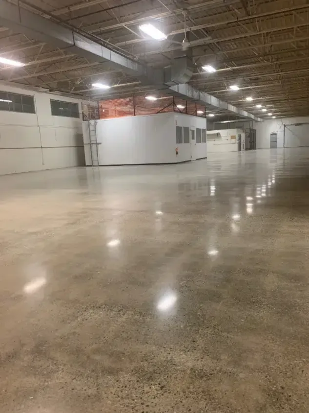 Empty warehouse interior with polished concrete floor, white walls, and overhead lights.