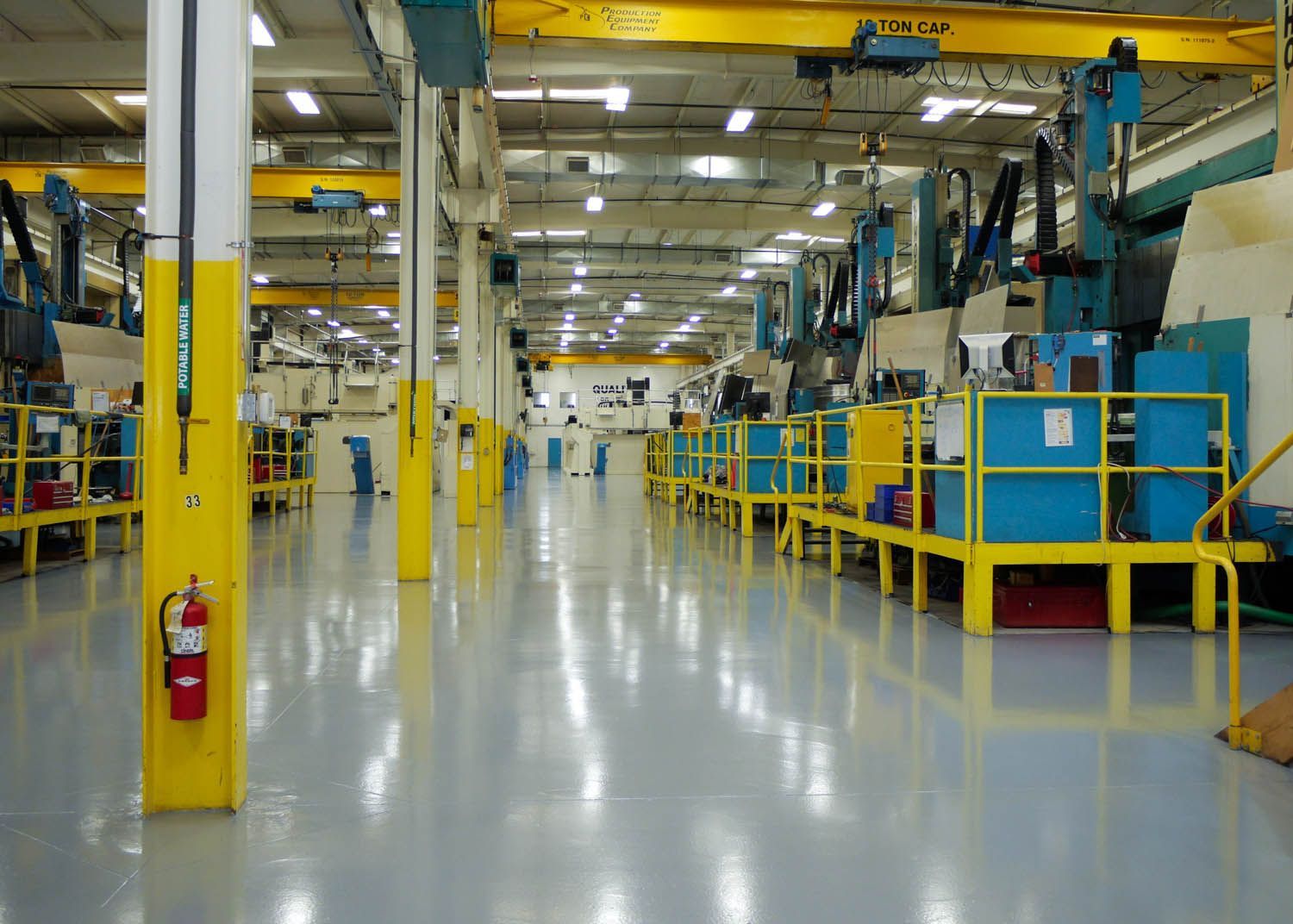 Bright factory floor with yellow railings, blue machinery, and polished concrete aisles