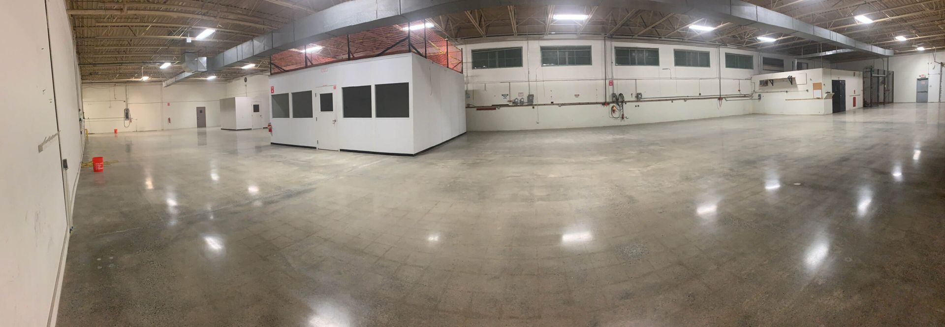 Wide empty warehouse with polished concrete floor, white walls, and exposed ceiling beams