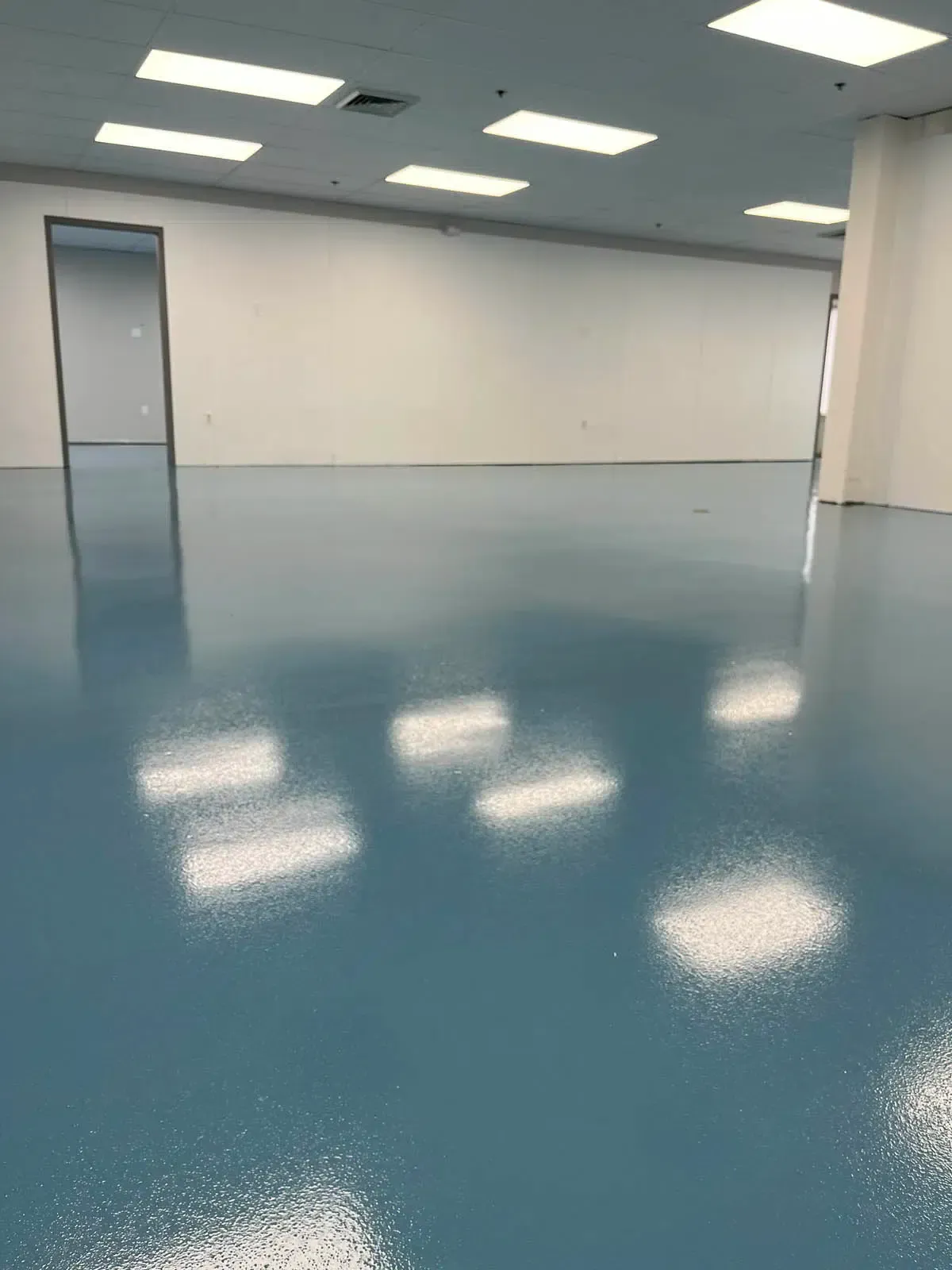 Empty blue-floored room with white walls and ceiling lights reflected on the floor