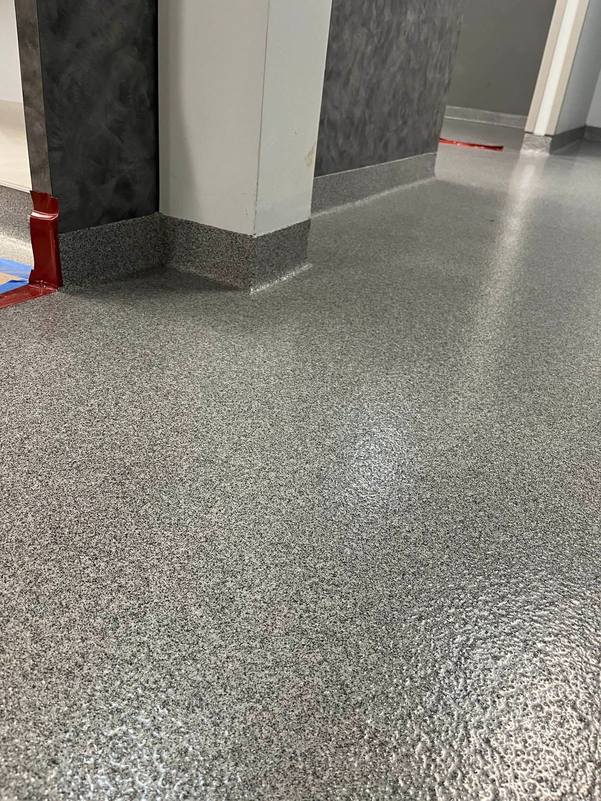 Gray speckled hallway floor with white walls and a red cone at the left edge