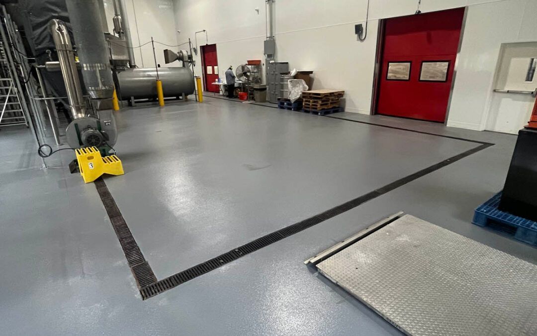 Industrial warehouse floor with a large gray epoxy-coated area and red doors in the background.