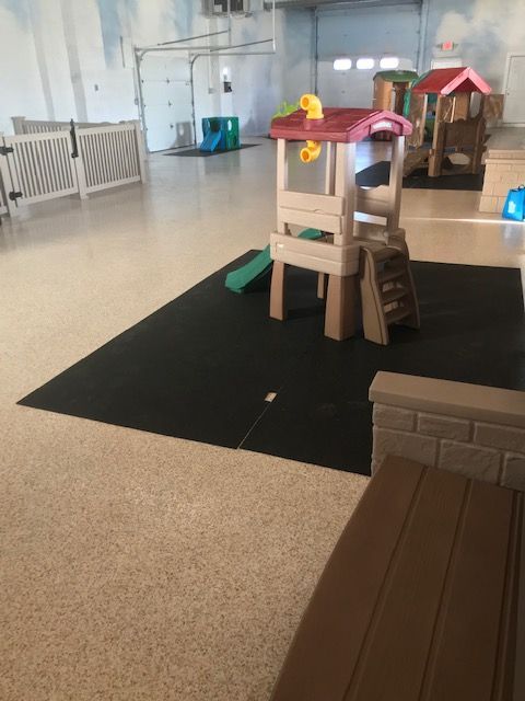 Indoor play area with toy playhouse, slide, black mat, and fenced toddler section