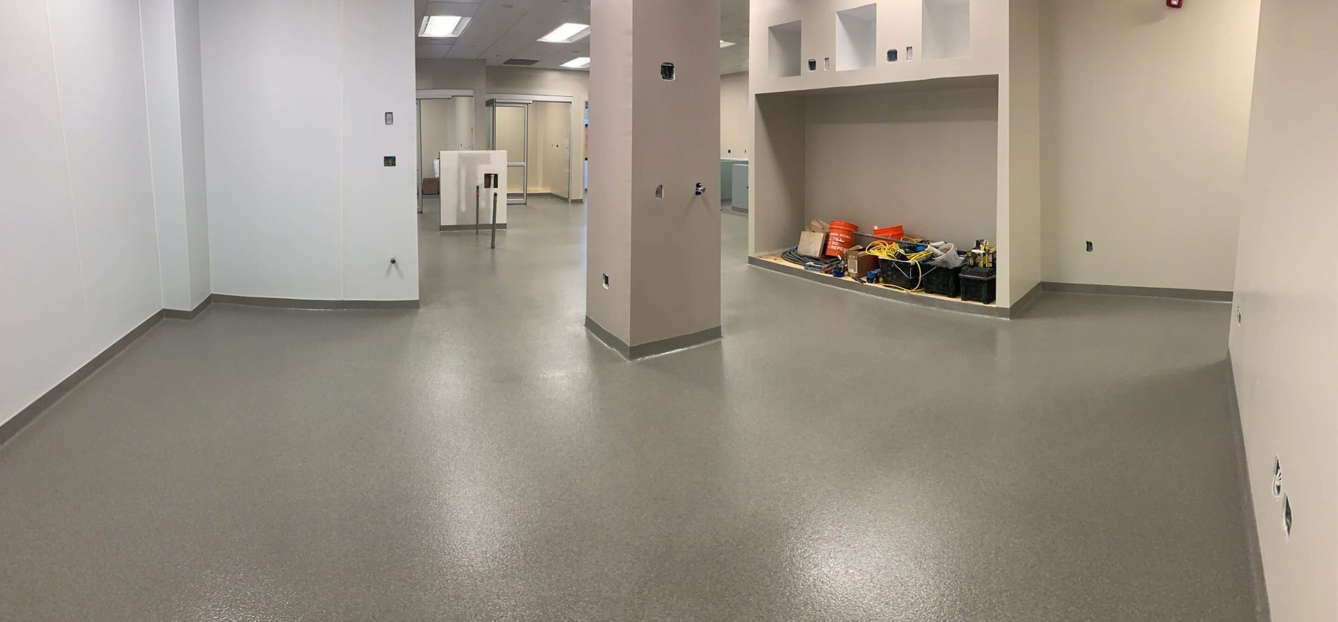 Empty gray indoor room with white cabinets, pillars, and a recessed shelf holding assorted items.