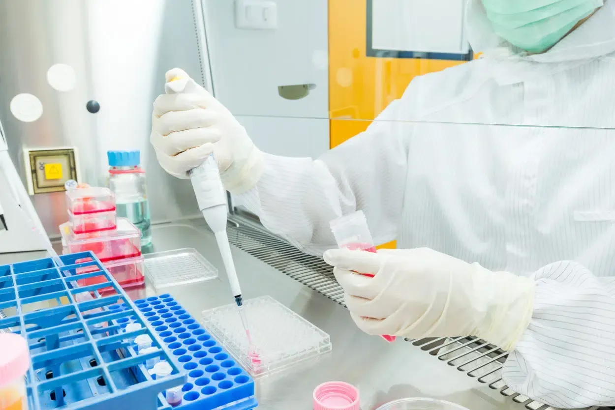 Lab technician pipetting samples in a clean laboratory with colorful test tubes and petri dishes