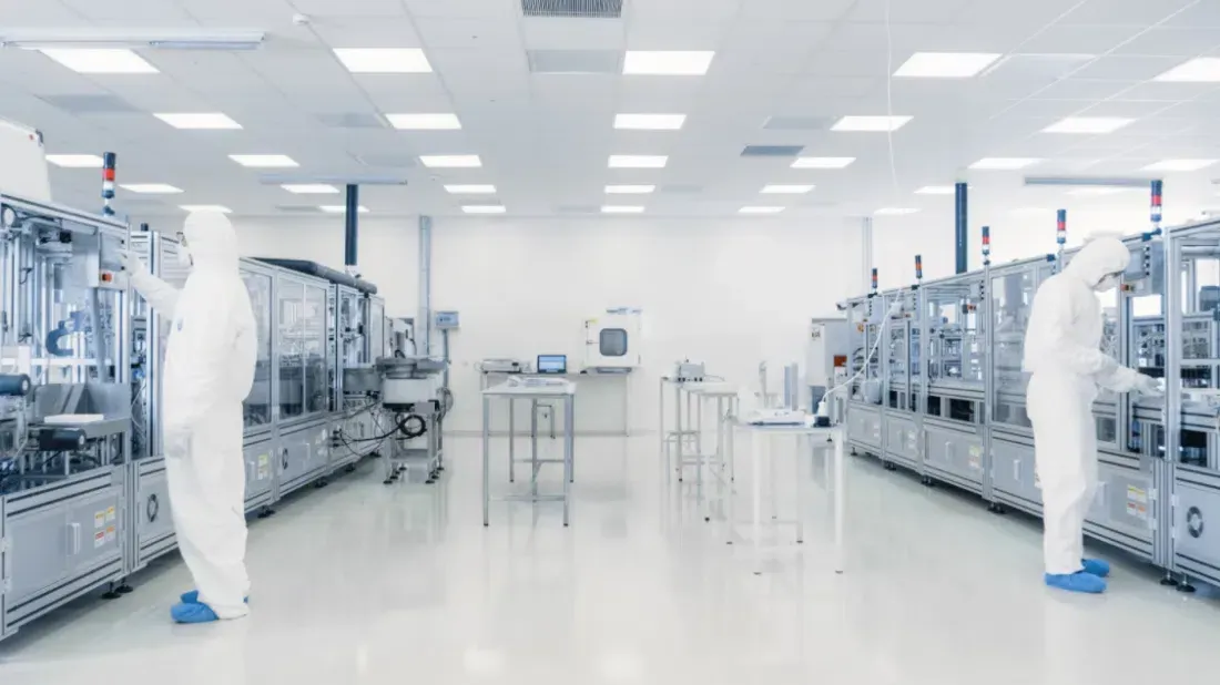 Bright cleanroom with two people in white protective suits working among industrial equipment under bright lights