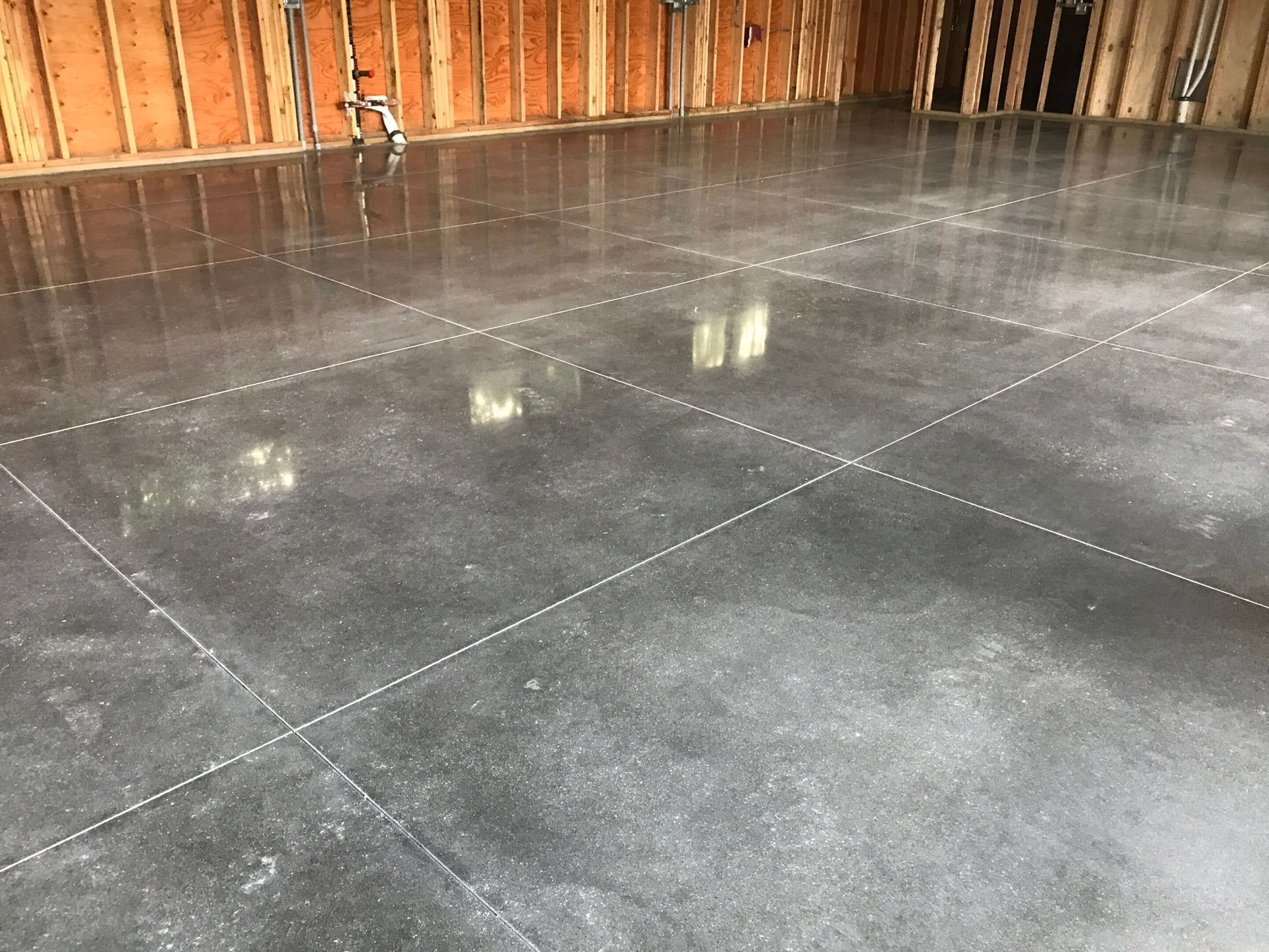 Empty unfinished room with a smooth gray concrete floor and exposed wooden walls.