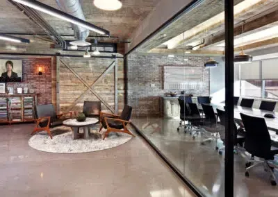 Modern loft office with glass walls, exposed brick, lounge seating, and a conference room with black chairs