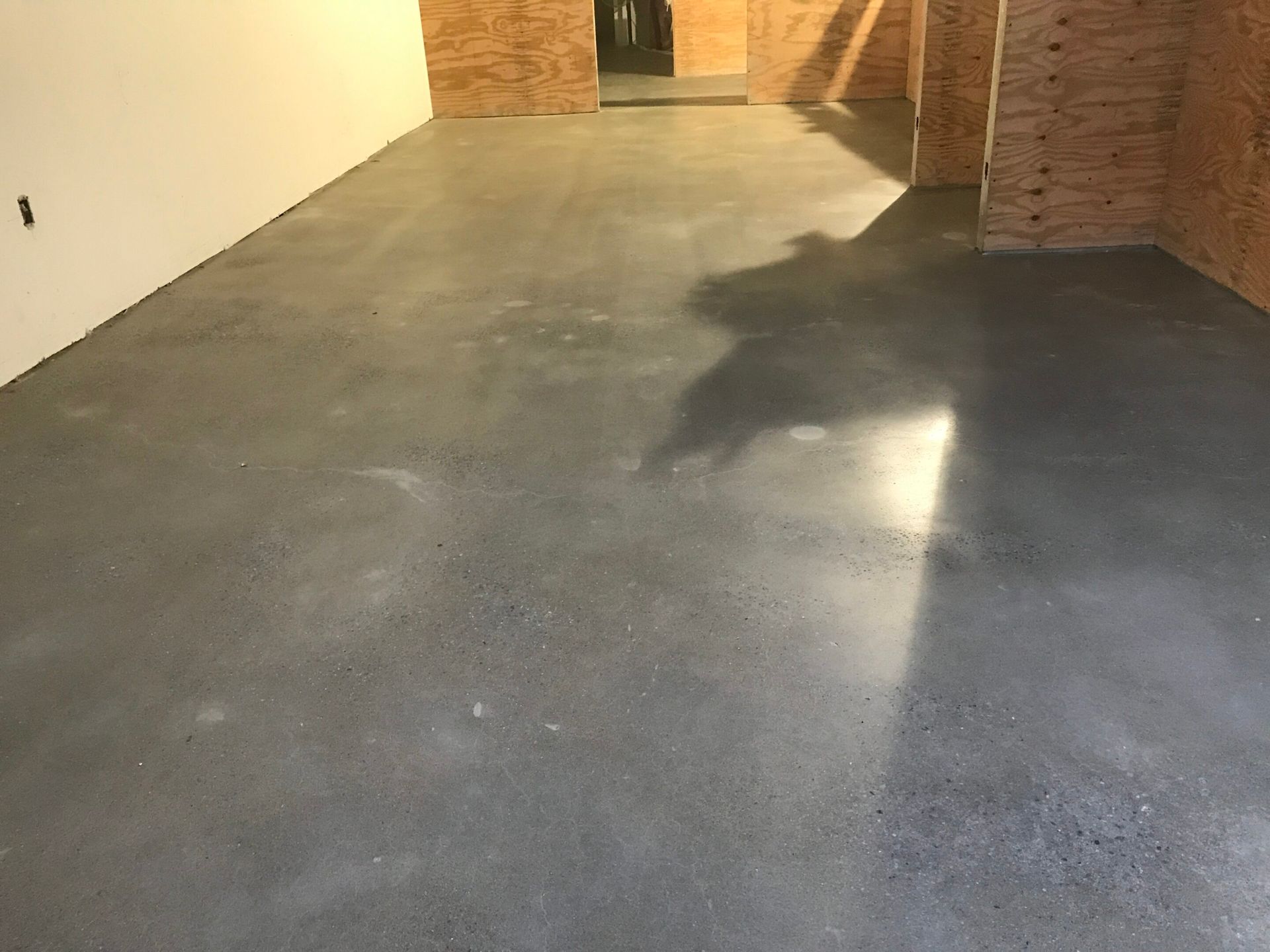 Empty concrete-floored room with brick walls and a white wall, lit by overhead light.