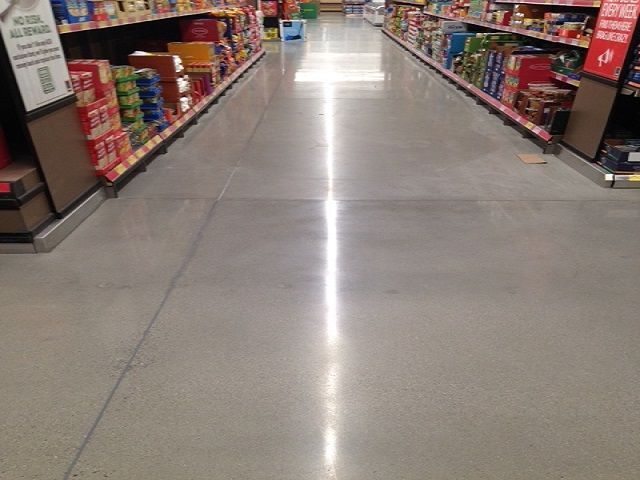 A supermarket aisle with shelves of goods on both sides and a polished floor reflecting overhead lights.