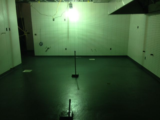 Empty green-tiled room with a dark floor, a hanging light, and a stand in the center.