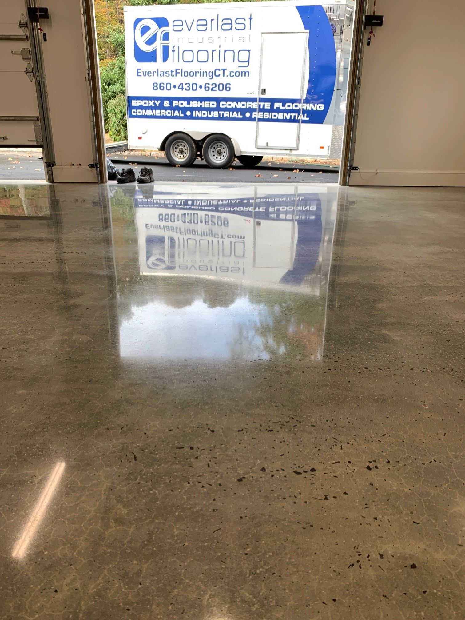 White Everlast Roofing trailer in a garage, reflected on a wet concrete floor.