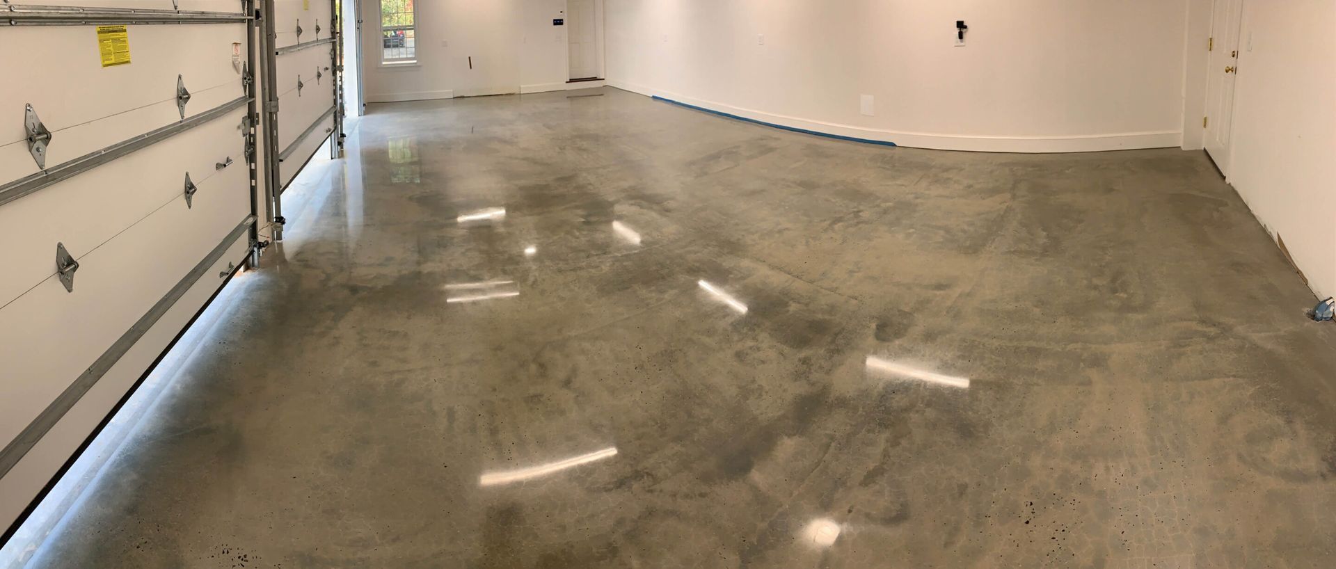 Empty garage with a wet concrete floor and white walls, viewed from the garage door
