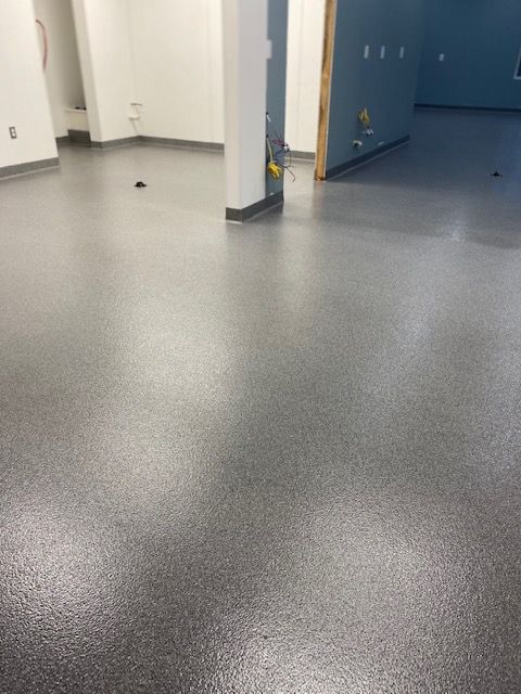 Empty indoor hallway with gray speckled floor, white walls, and blue doors.