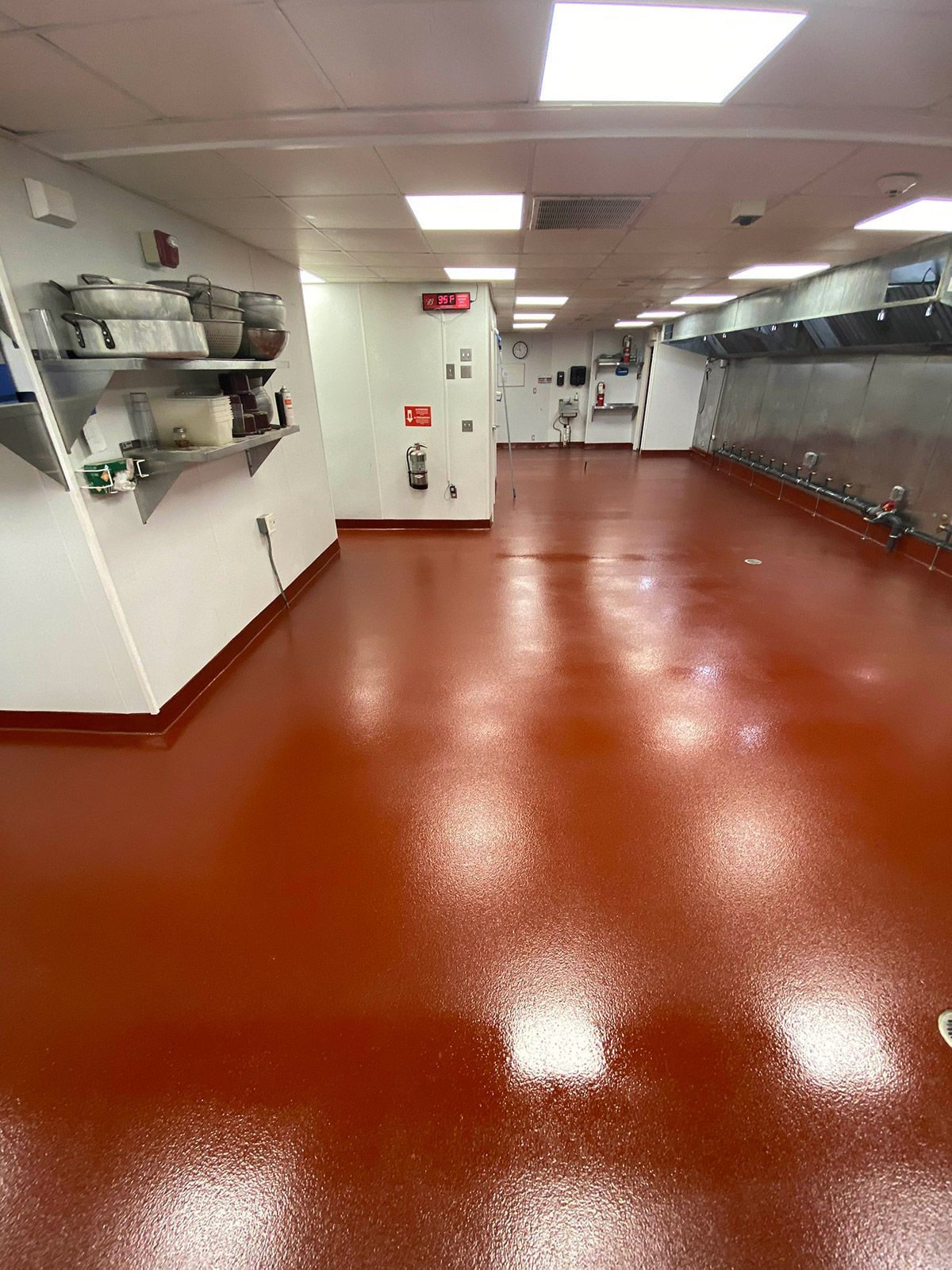 Empty industrial kitchen with red floor, stainless steel counters, and white ceiling lights