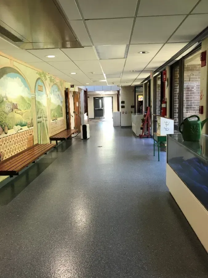 Empty hallway with mural-lined walls, overhead fluorescent lights, and polished dark floor.