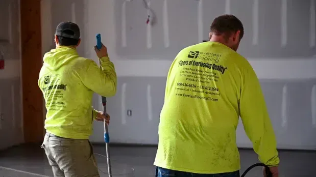 Two workers in neon yellow shirts painting a gray interior wall with rollers