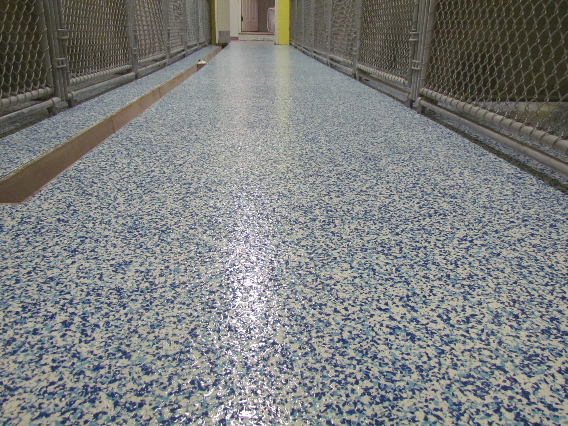 Long, empty walkway with blue-speckled floor and chain-link fencing on both sides