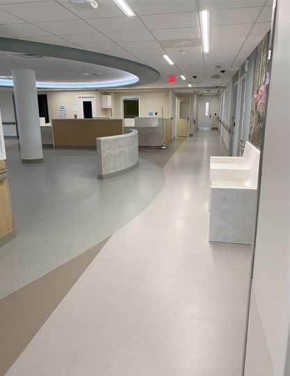 Empty hospital corridor with white floors, reception desks, and overhead lighting