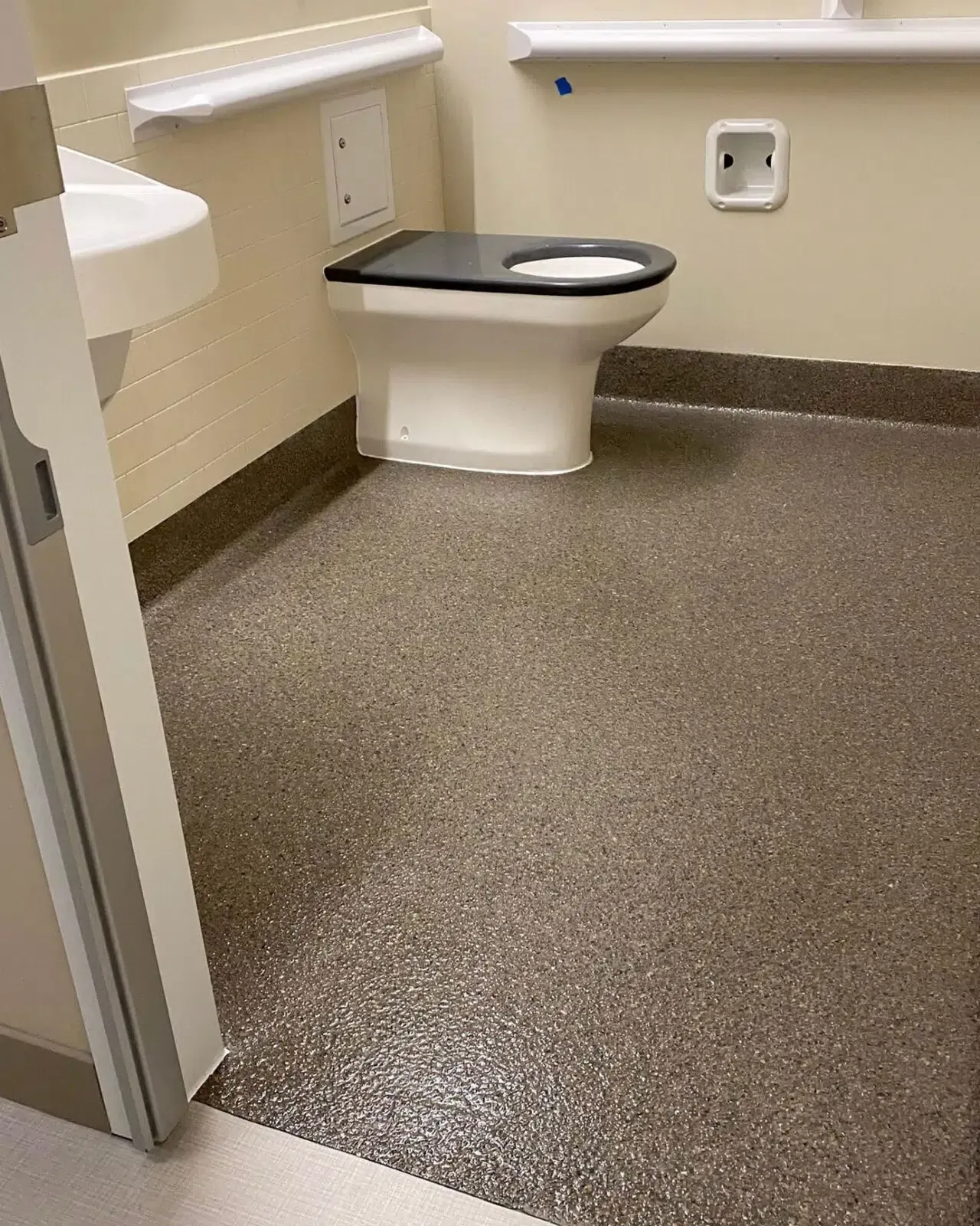 Accessible restroom with a toilet, wall grab bars, and a speckled non-slip floor