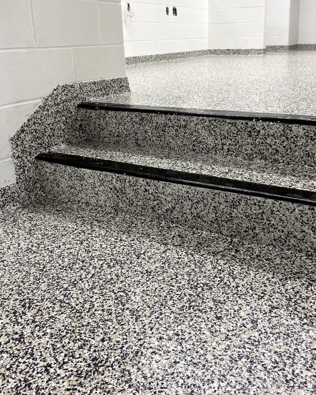 Speckled terrazzo stairs with black edge strips in a white hallway
