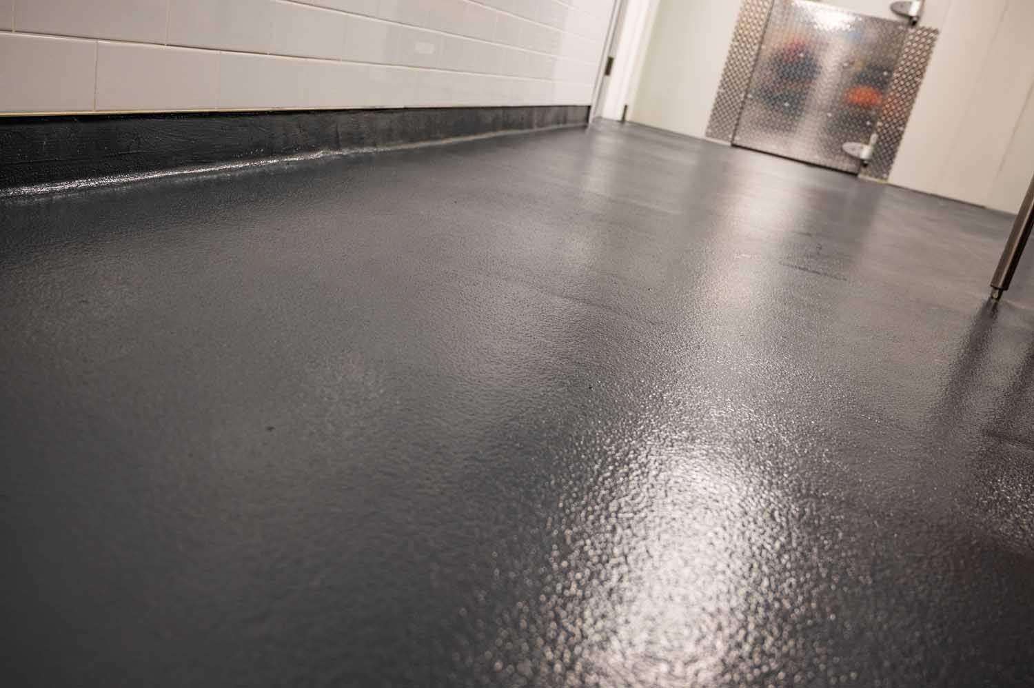 Empty hallway with a dark, wet floor and white walls leading to a metal door.