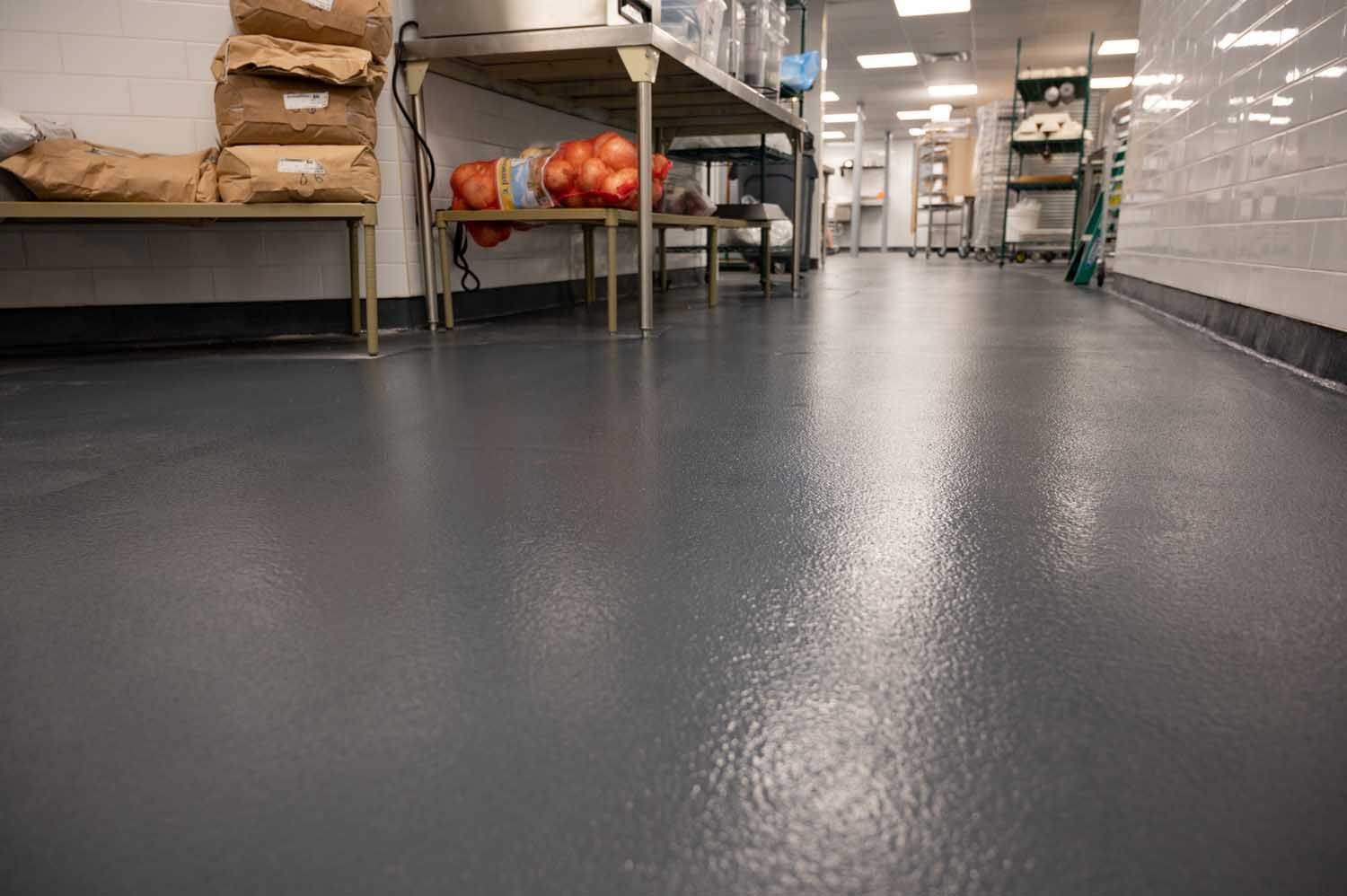 Empty industrial kitchen with a dark epoxy floor and metal shelving along the walls