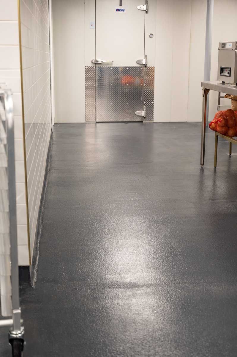 Empty hallway with glossy black floor, white walls, and a metal gate at the far end