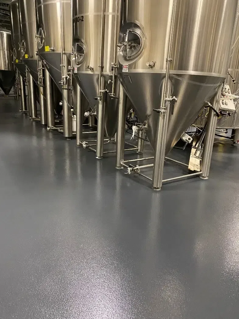 Stainless steel industrial tanks and hoppers in a clean factory room with a gray epoxy floor