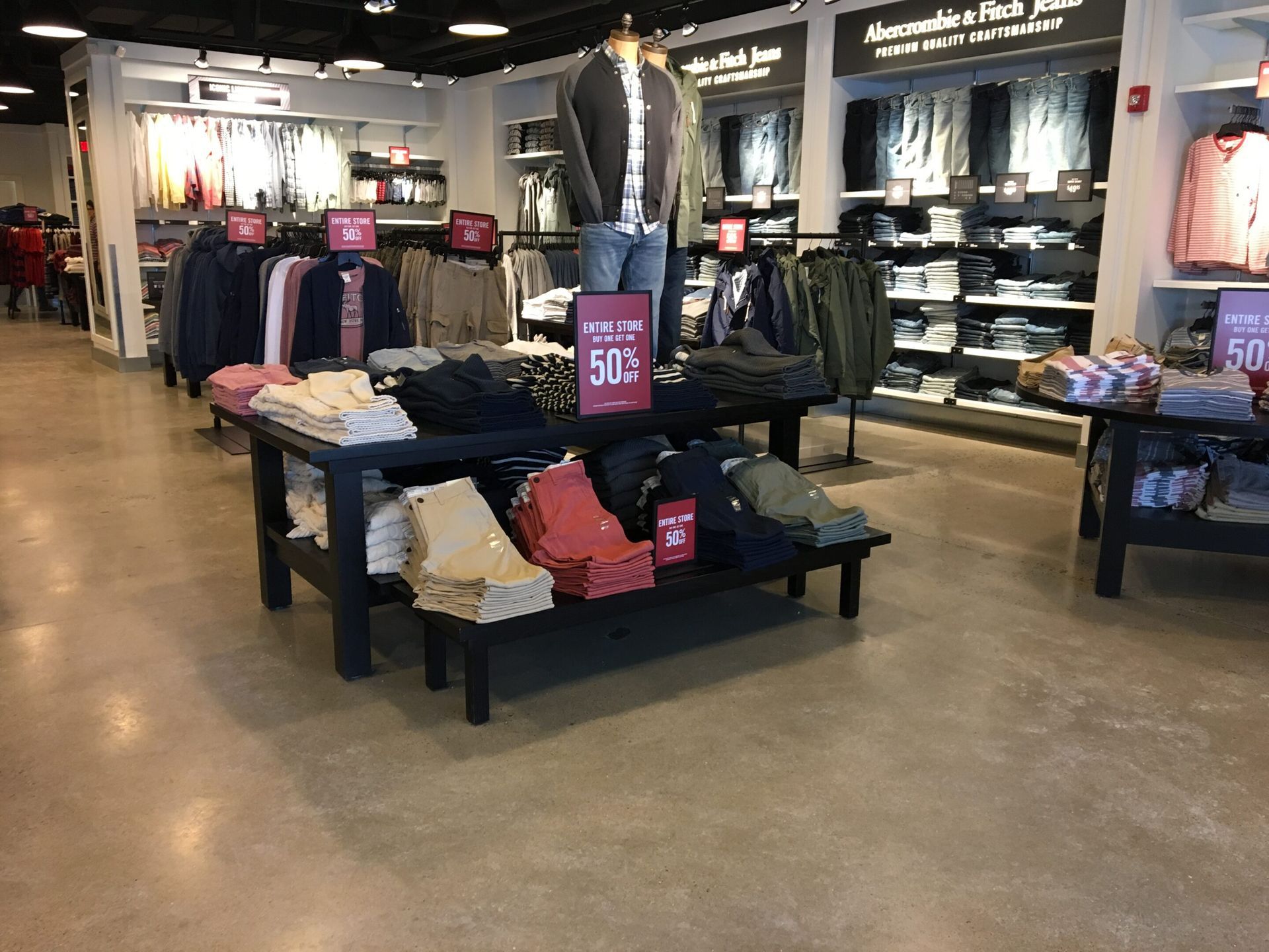 Clothing store interior with racks of apparel, folded shirts, and sale signs under bright lights