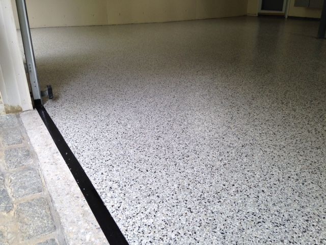 Empty indoor hallway with a speckled gray floor and a black border along the edge