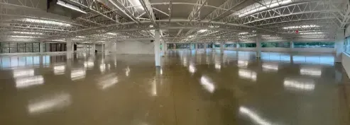 Empty indoor warehouse with polished floor, steel beams, and bright skylights across the ceiling