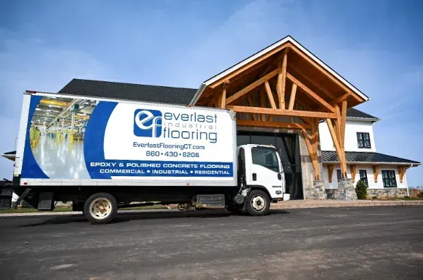Delivery truck with Everlast Flooring logo parked outside a large wooden building
