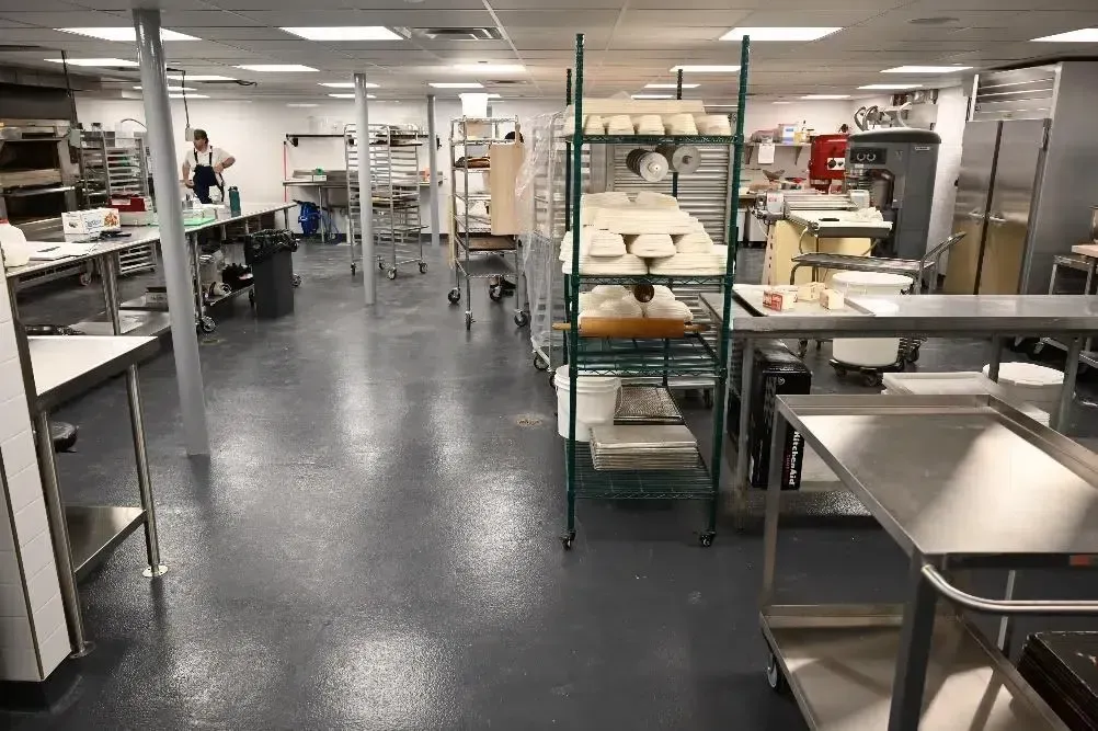 Commercial kitchen with stainless steel prep tables, shelving, and equipment in a bright room