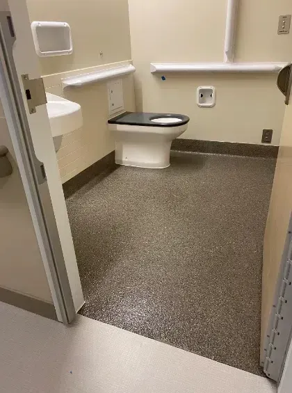 Accessible restroom with toilet, grab bars, and sink in a beige-tiled room