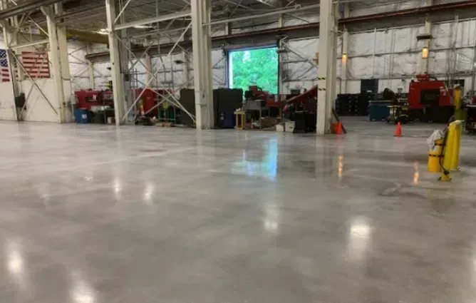 Large empty warehouse floor with industrial equipment and orange safety cones along the walls