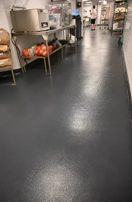 Commercial kitchen with stainless steel counters, black floor, and baskets of oranges on the left.
