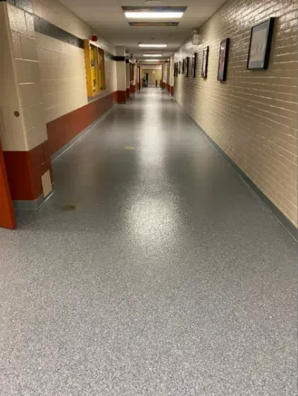 Empty school hallway with beige walls, gray floor, and framed pictures on the right.