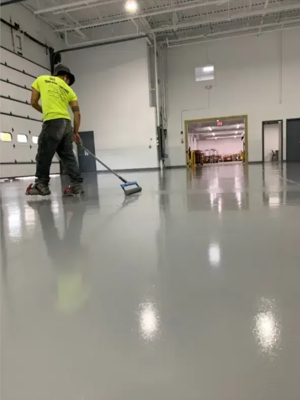 Worker in a neon shirt mops a glossy warehouse floor near an open loading bay.