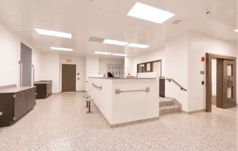 Empty hospital reception area with white counters, beige walls, and bright overhead lights