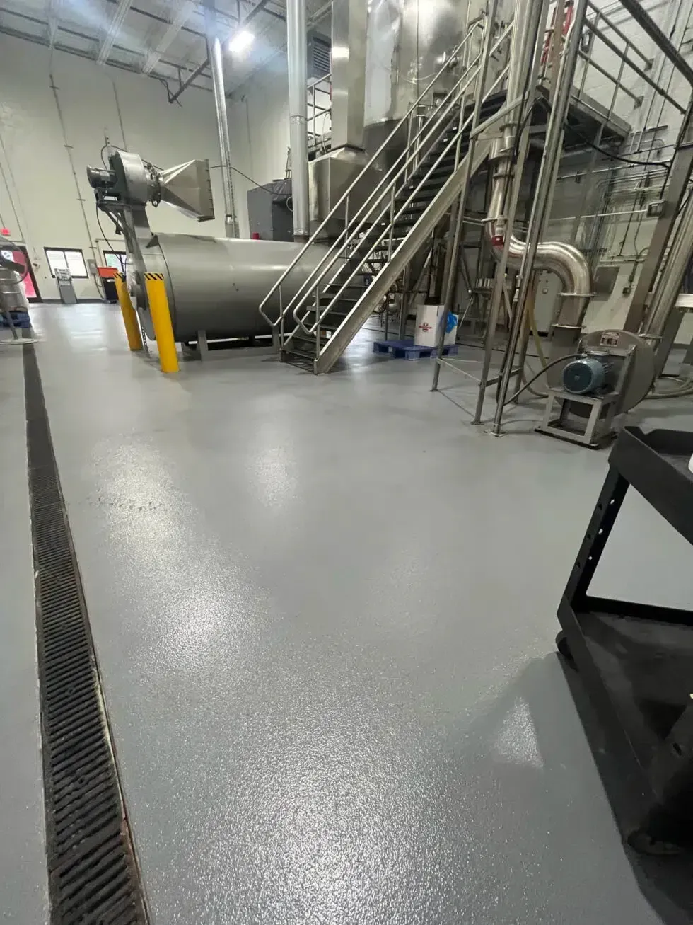 Industrial factory floor with metal stairs, pipes, and gray machinery on a polished concrete floor