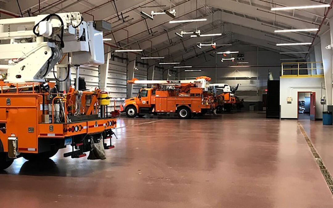 Orange utility trucks parked inside a large industrial garage with a high arched ceiling