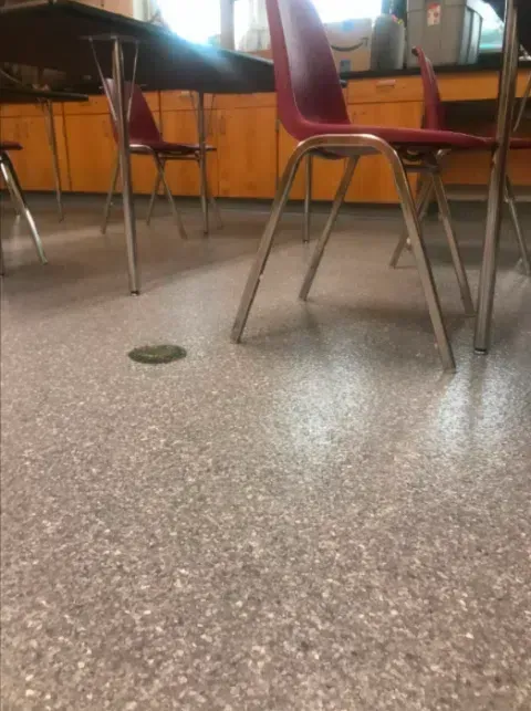 Classroom floor with red chairs and metal desk legs on speckled linoleum.