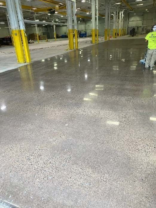 Shiny polished warehouse floor with yellow columns and a worker in a neon jacket