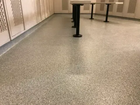 Empty locker room with beige lockers, speckled floor, and metal table legs
