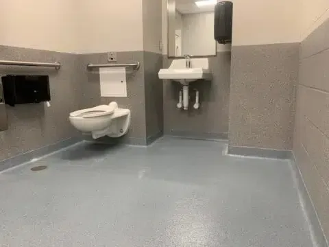 Accessible restroom with wall-mounted toilet, sink, grab bars, and gray flooring