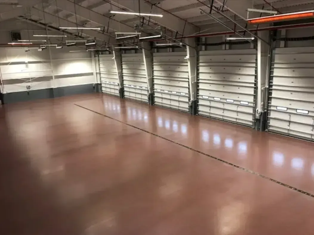 Empty indoor warehouse with a polished brown floor and tall white walls under overhead lights